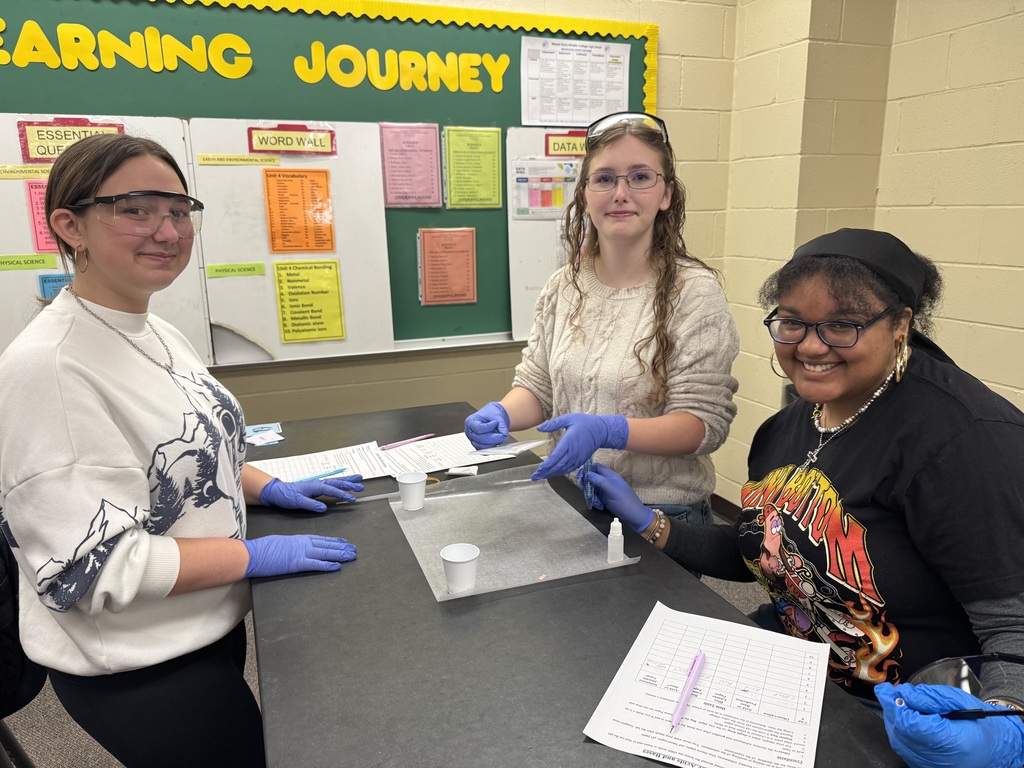 Three girls experimenting on a science table with acids and bases in class.