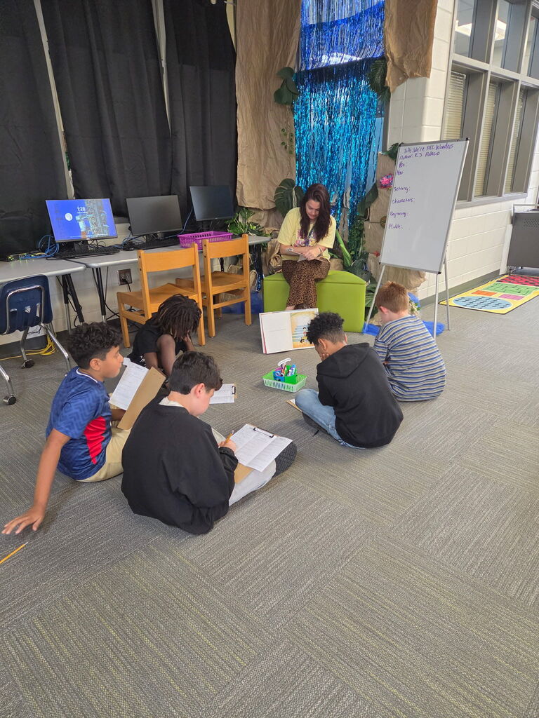 A teacher reads to a group of children seated on the floor in a classroom.