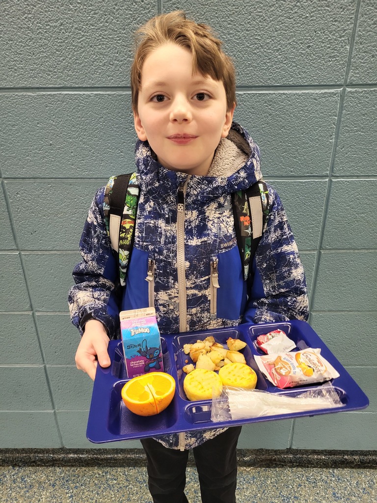 Elementary age student holding a tray with breakfast containing milk, orange, potatoes and egg bites.