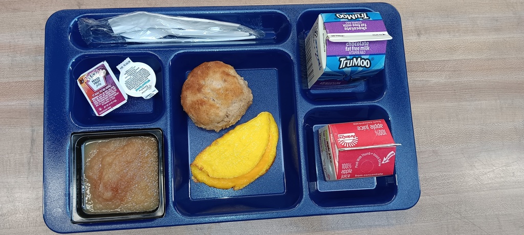 Blue lunch tray on a table with egg and cheese omelette with a biscuit, cinnamon applesauce, juice and milk on it.