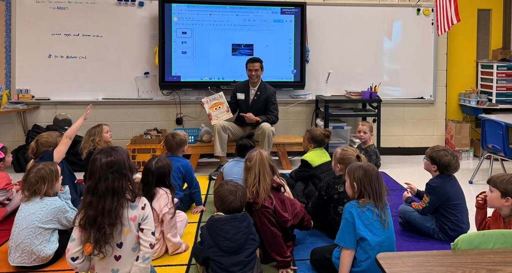 Read Across America. Several students sitting down while someone reads a book to them.