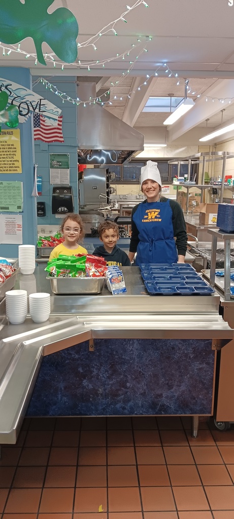 volunteer with two small children standing behind a counter to serve breakfast