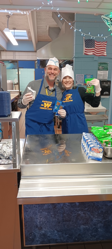 Two volunteers with gloves on holding up food and smiling behind the camera.
