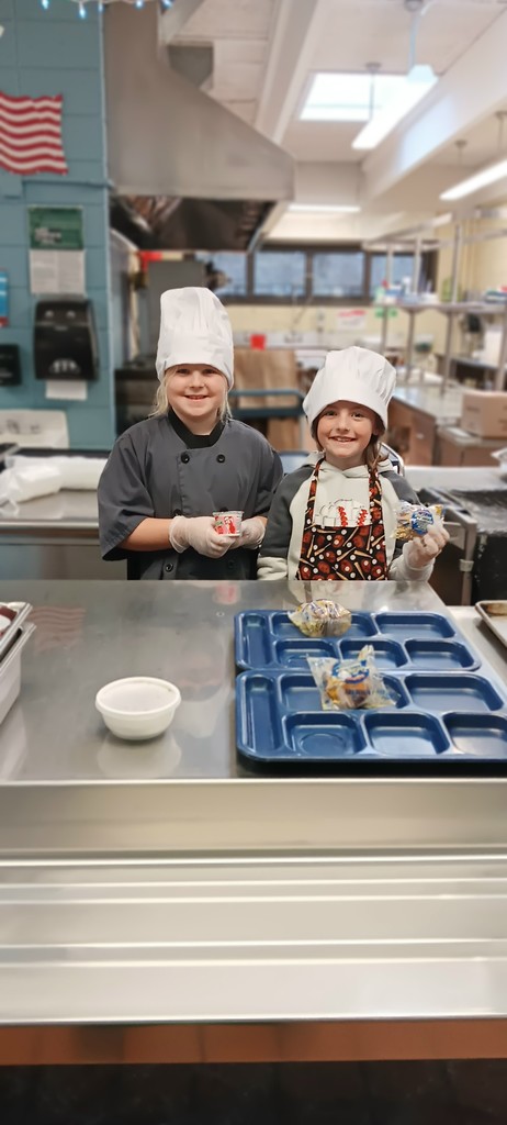 One boy and one girl wearing chef hats and gloves about to serve food
