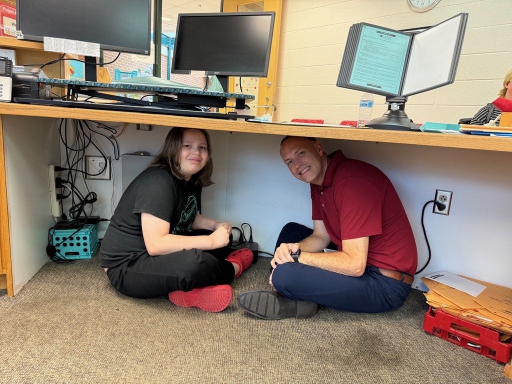 Dr. Ryan Barber and a Waynesboro Public Schools student take cover under a table during the Great ShakeOut earthquake preparedness drill, practicing the “Drop, Cover, and Hold On” safety procedure.