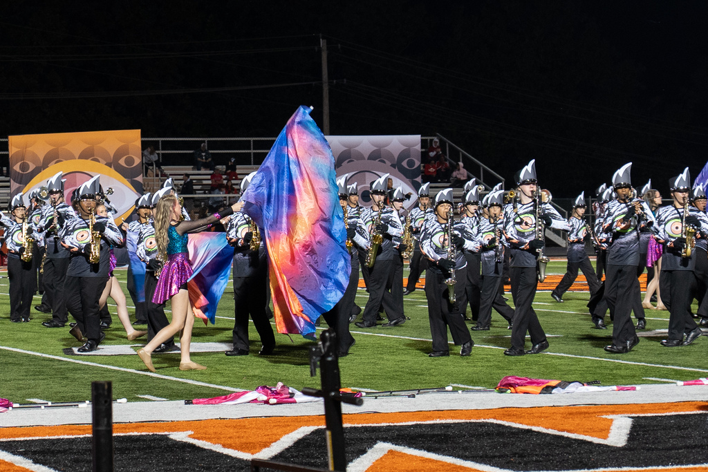 Marching band performing on a football field with the Guard member carrying multiple color flag 