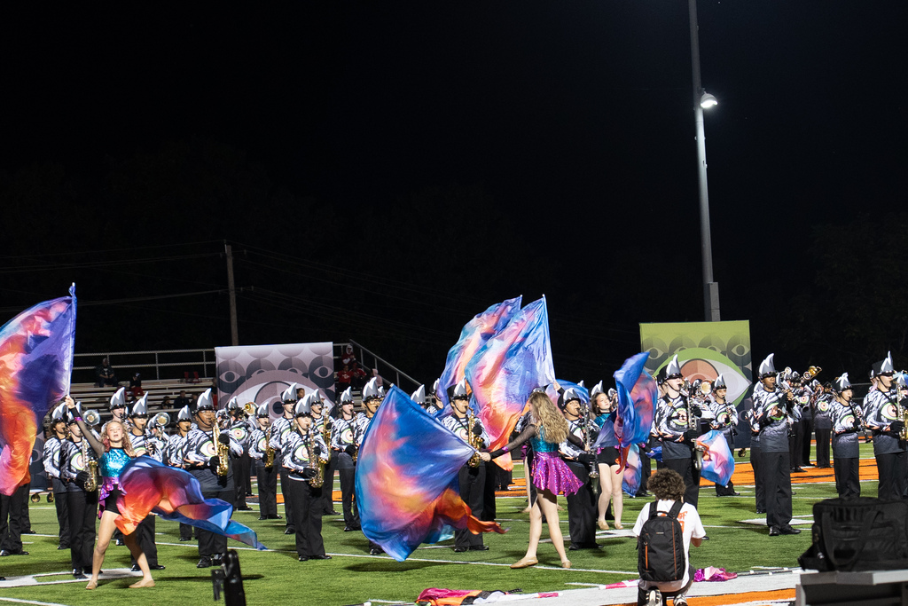 Marching band performing on a football field with Guard members putting  multiple color flags in the air