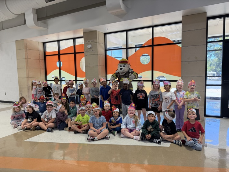 36 students standing with the fire dog (mascot) posing for a picture with their paper colored fire hat headbands