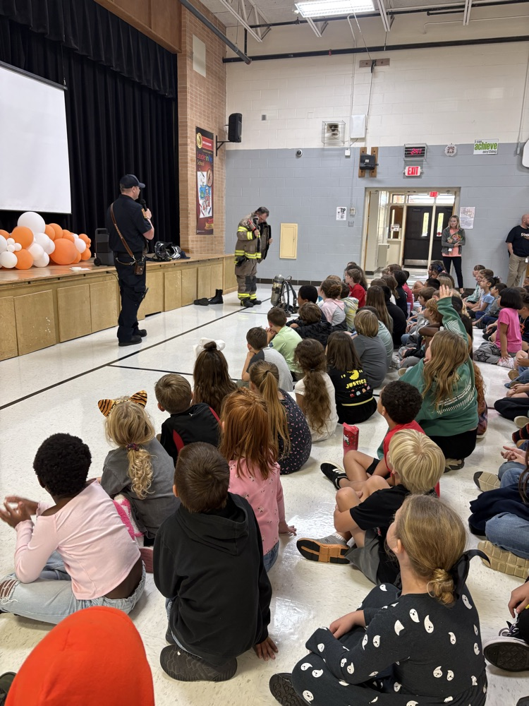 Students sitting and watching a firefighter put on their gear.