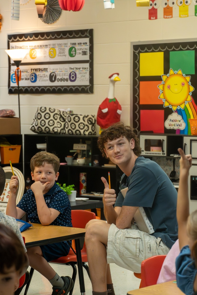 A male high school student engaging in the kindergarten class activities with the little kids around him.