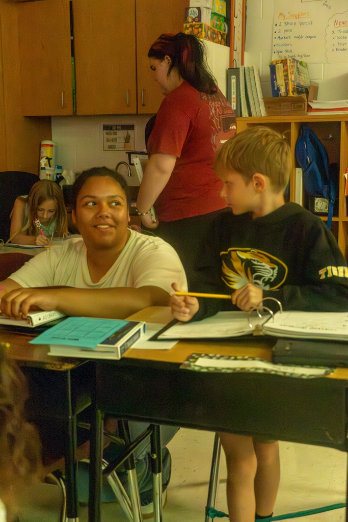 A female high school student helping a little boy write his two paragraphs.