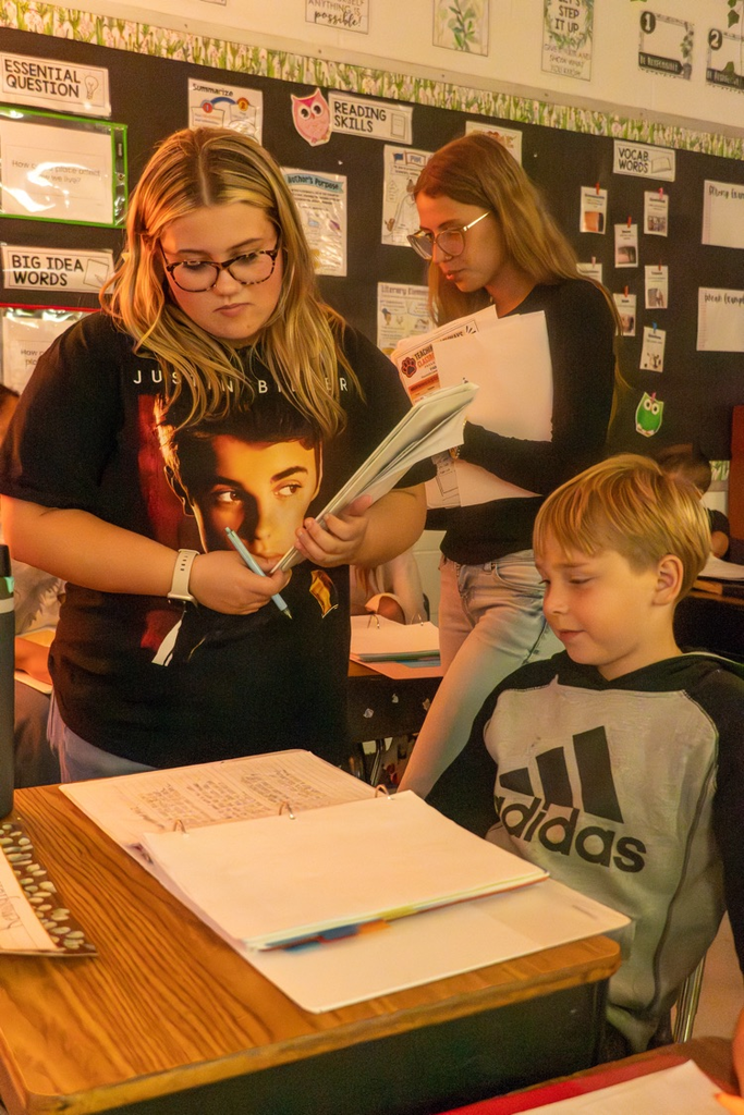 A female student asking a fourth grader whatās heās writing about.