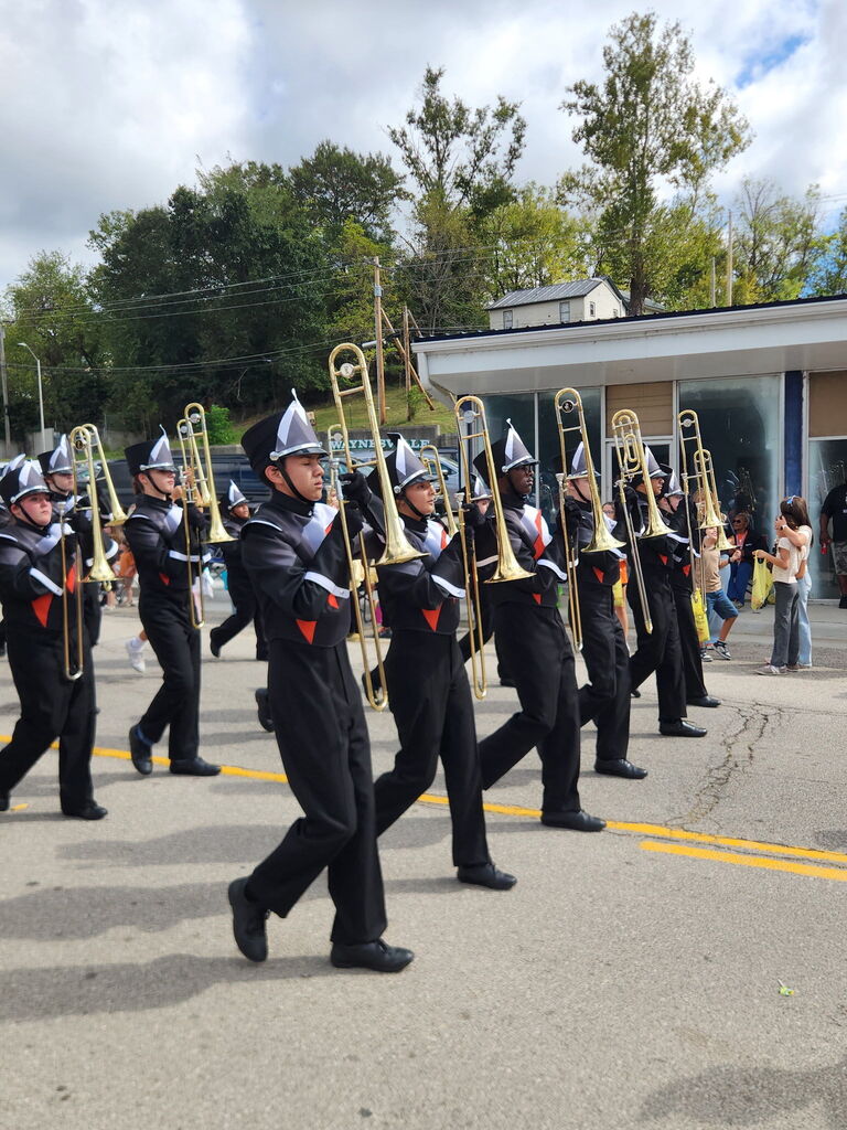 Band students who play the trombone marching in uniforms on a street