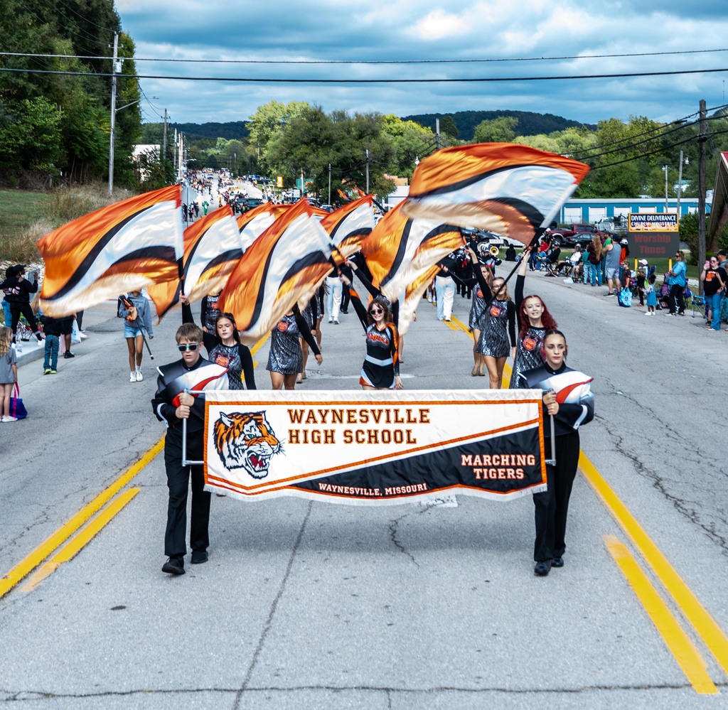 Waynesville High School band banner with color guard behind them with their in the air.