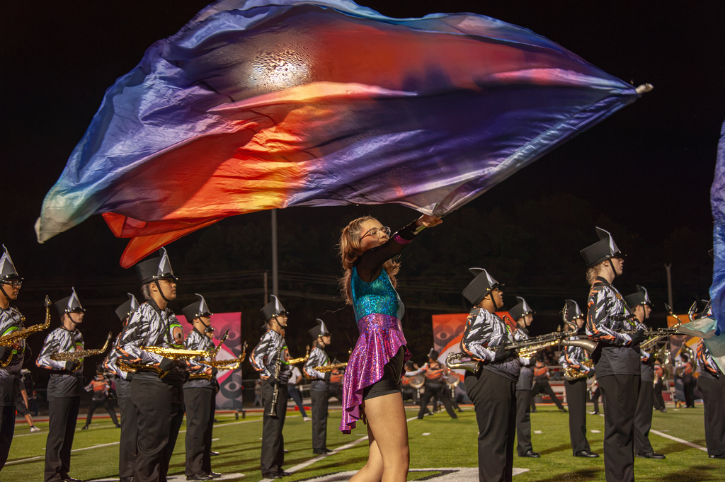 Pretty purple, pink, and orange flag in the air being held by a female color guard student.