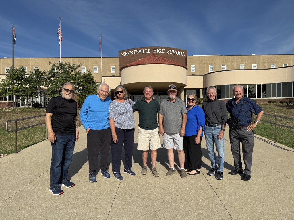Eight members of the Class of 1966 standing in front of the current high school.