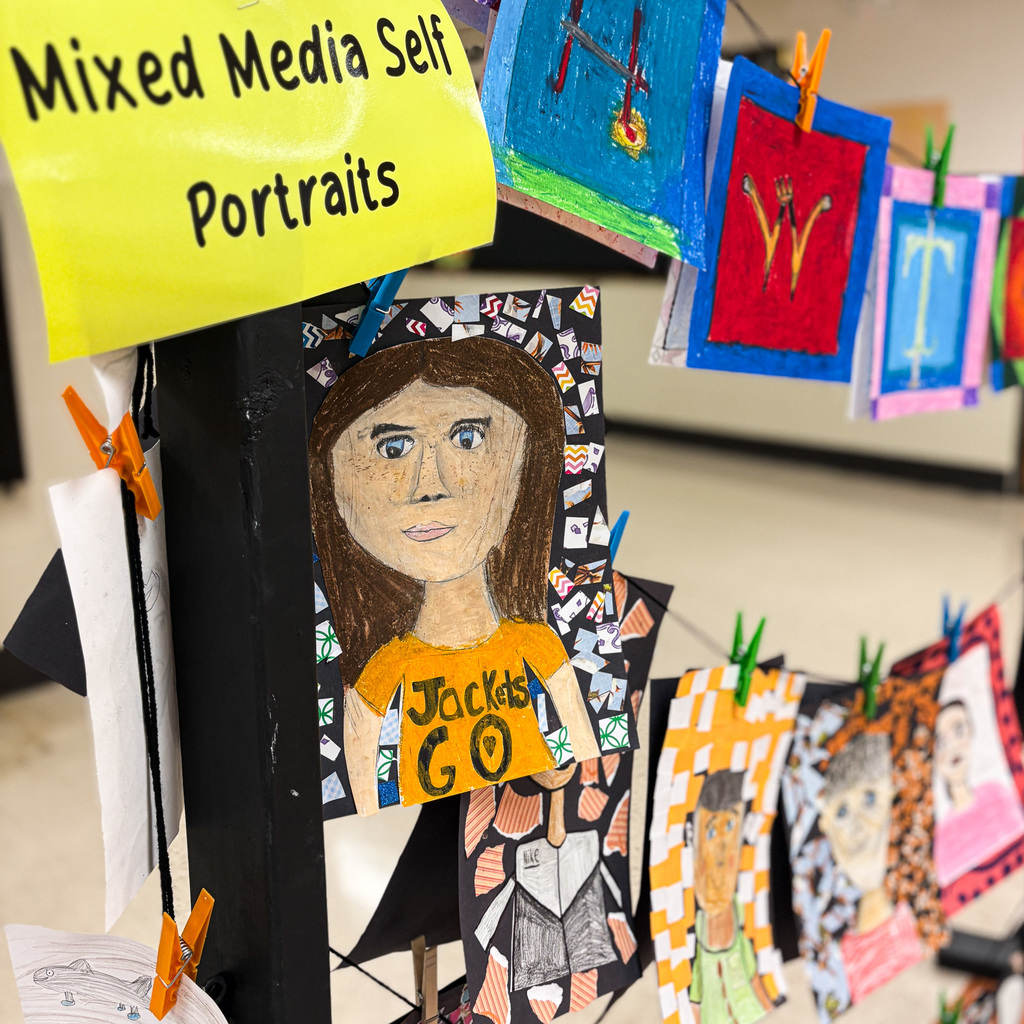 Art project display with mixed media self-portraits hanging on a line with clips, including one portrait of a girl.