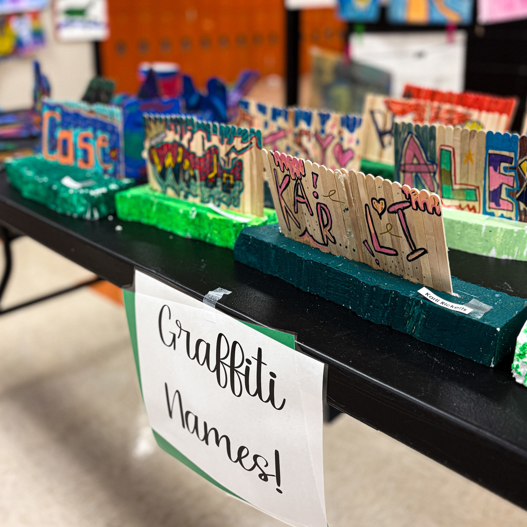Display table with various graffiti-themed art pieces on green bases. A sign reads "Graffiti Names!" Brightly colored art pieces in various styles.