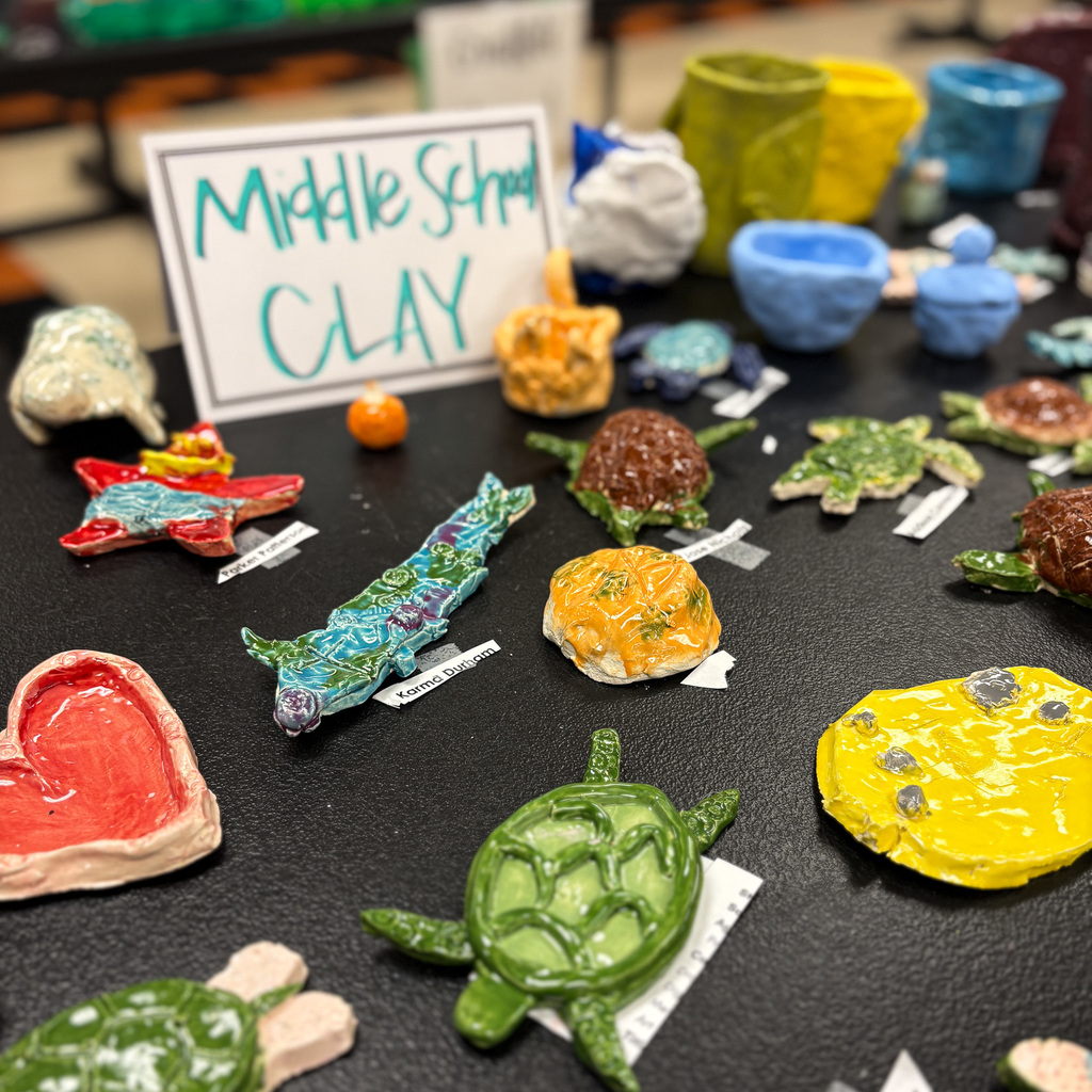 Display of various clay sculptures including turtles, a crocodile, and a heart on a table.