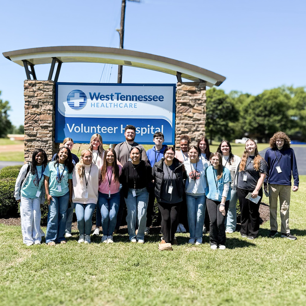 A group of people pose in front of a hospital sign in a grassy field.