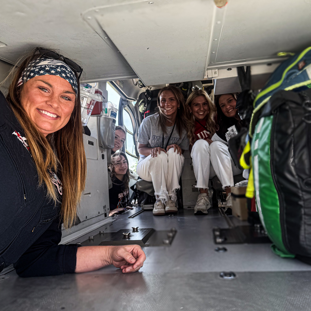 Five people inside a helicopter, two sitting on the floor, one leaning against a wall, and others seated.