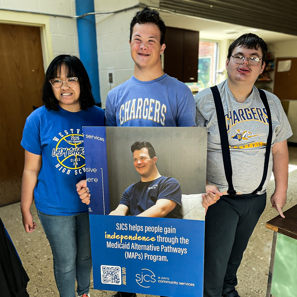 Three people stand with a poster, one person holds a sign that features a photo of a man.