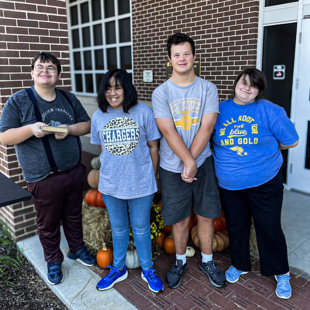Five people stand outside a brick building, smiling. They are dressed casually. A pumpkin display is behind them.