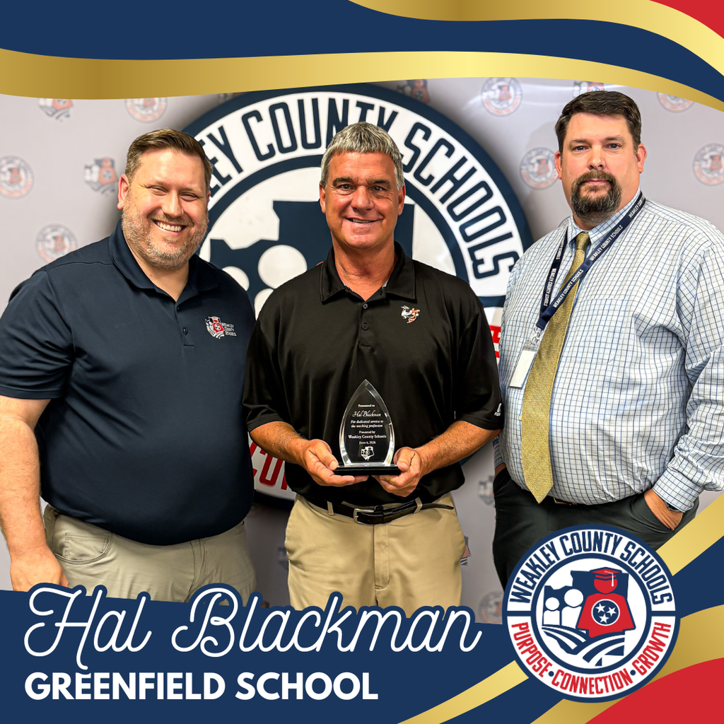 Three men stand in front of a school logo backdrop. The center man holds a trophy, and the others smile.