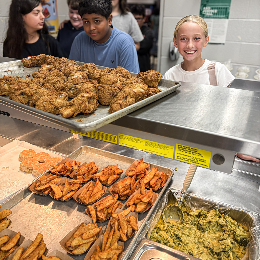 A group of kids at a lunch counter with trays of food, including fried chicken, fries, and a green dish.