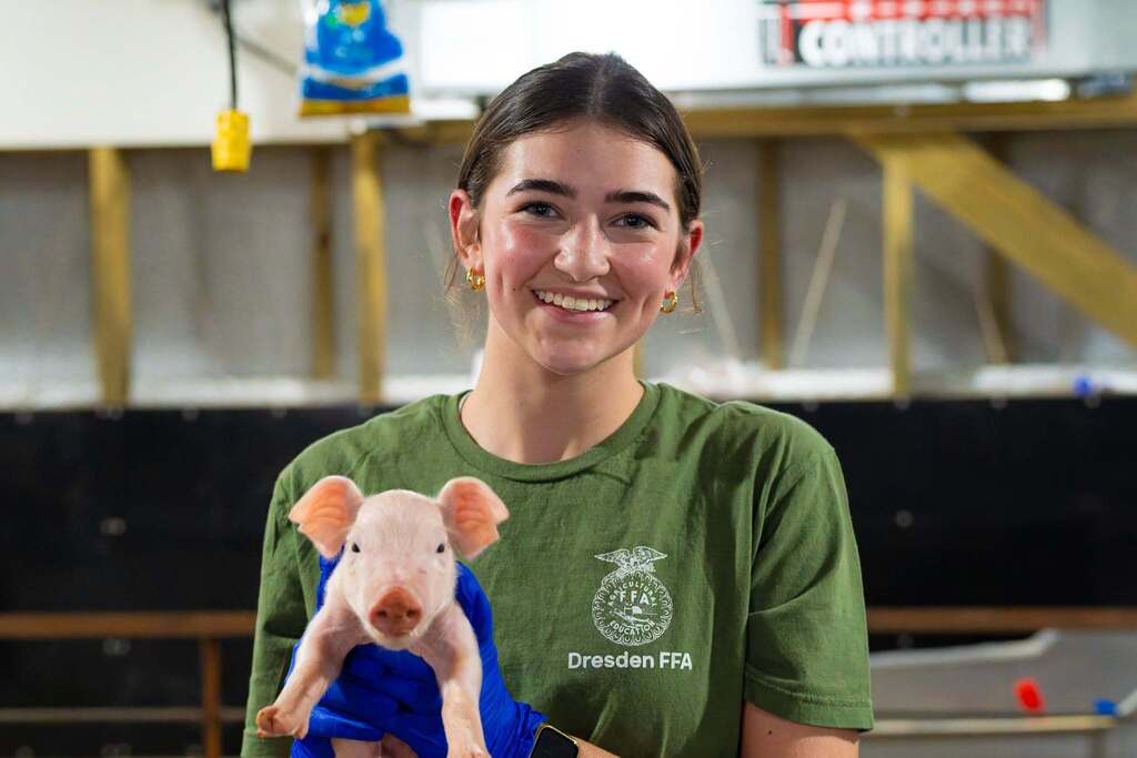 A woman with a green shirt smiles while holding a small pig in a lab setting.