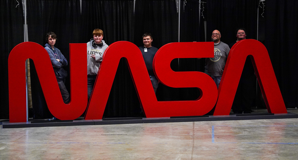 Dresden High School students and staff stand behind a large, freestanding red NASA logo during CTE Day at Marshall Space Flight Center.
