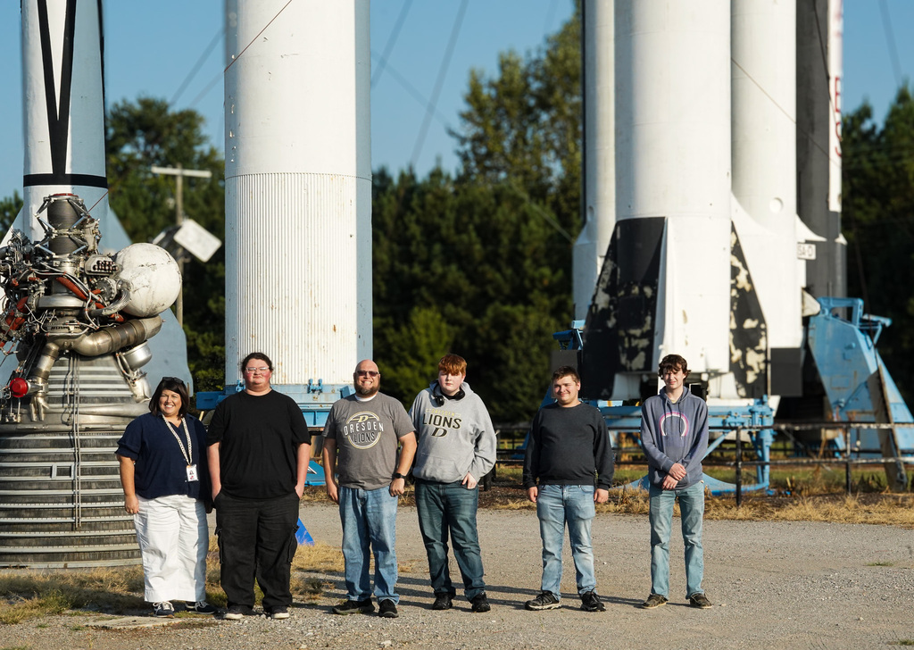Students and staff from Dresden High School pose outdoors at NASA’s Marshall Space Flight Center in front of large rocket and propulsion hardware.