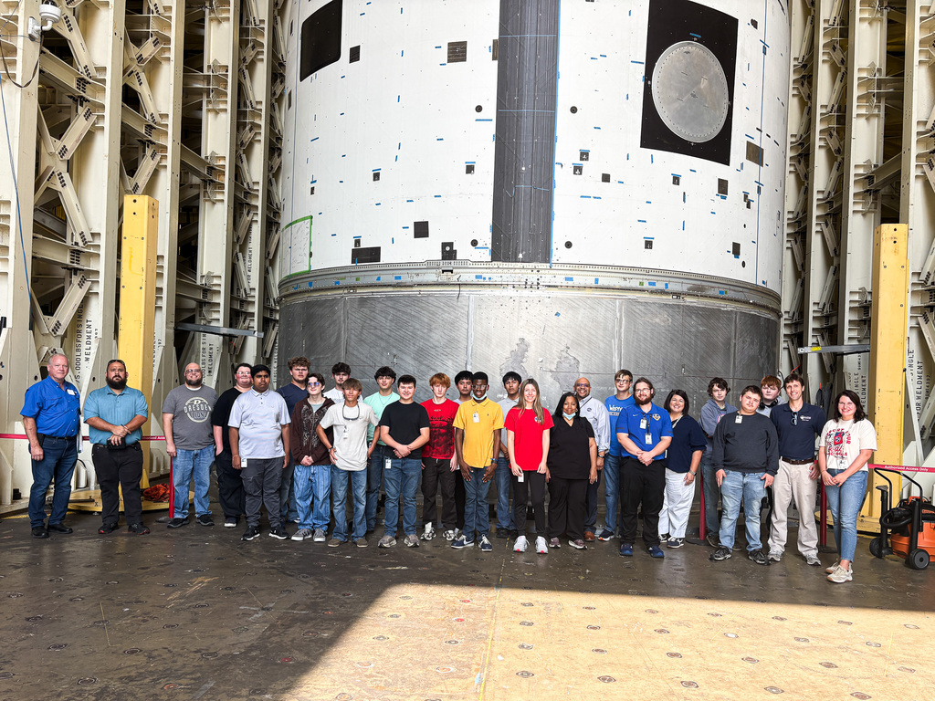 Dresden and Westview CTE students, teachers, and NASA staff pose together inside a Marshall Space Flight Center facility in front of a massive spacecraft component.