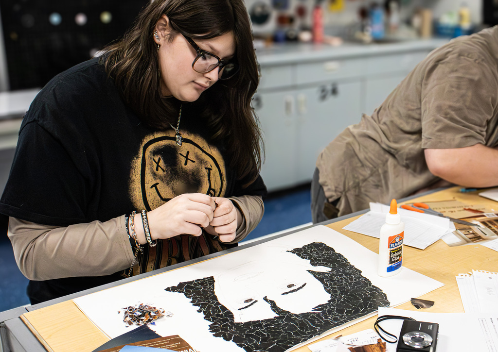 A Westview student concentrates on a black-and-white portrait mosaic, filling the subject’s dark hair and clothing with many small pieces cut from magazine pages.