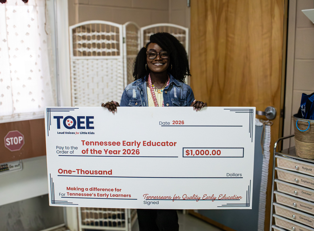 Michaela Frederick smiles in her classroom while holding an oversized $1,000 check recognizing her as a 2026 Tennessee Early Educator of the Year.