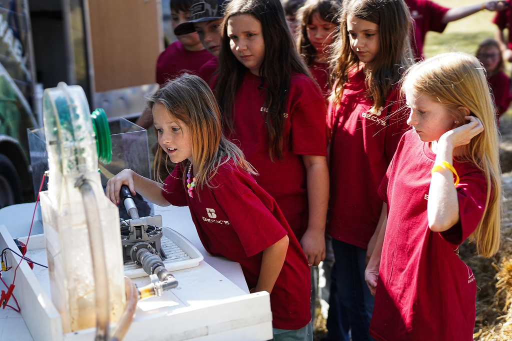 Group of children in red shirts gathered around an ag energy project on a table. 