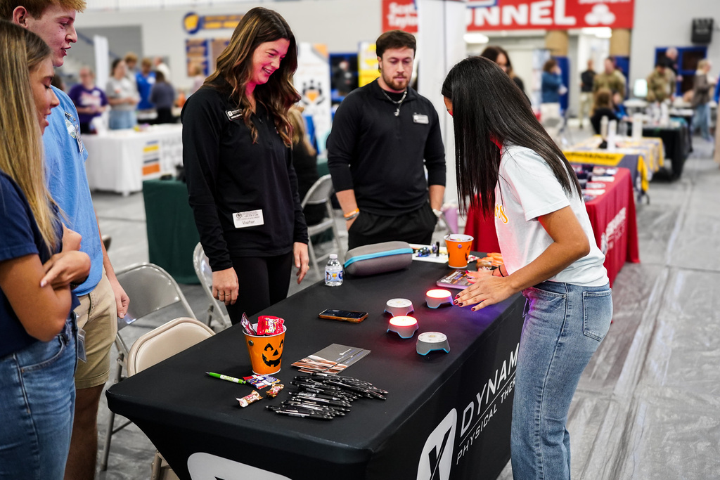 A group of people are gathered around a table with physical therapy career fair items on it. 