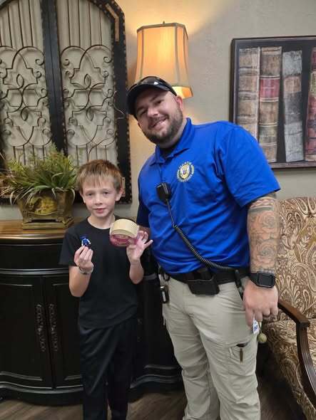 Man in uniform and boy holding badges stand next to each other in a room.