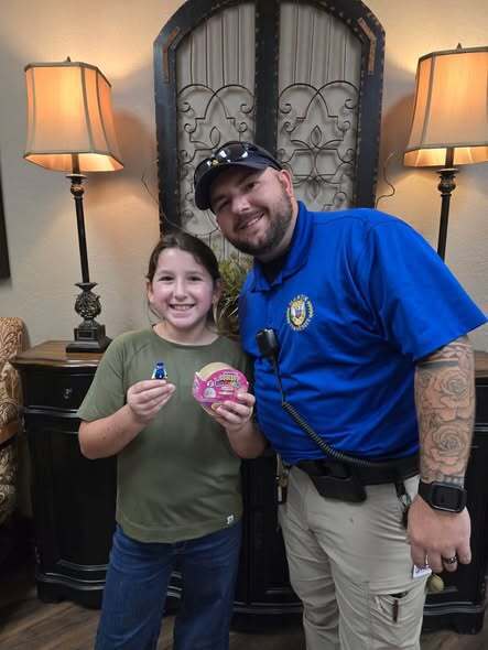 Man in blue uniform and woman in green shirt holding up pink items standing next to each other.