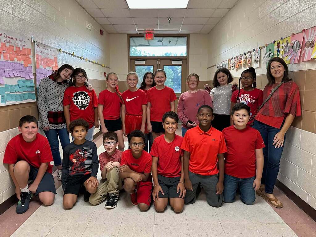 Elementary students and two staff members gather in a school hallway wearing red and red-accented clothing in support of Red Ribbon Week.