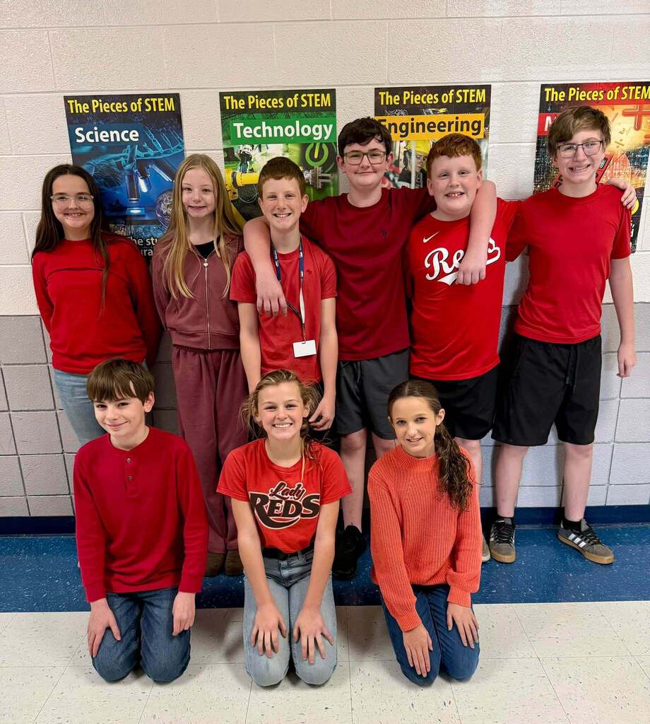 Nine middle school students pose together in a hallway wearing various shades of red, including T-shirts, sweatshirts, and athletic clothing, in recognition of Red Ribbon Week.