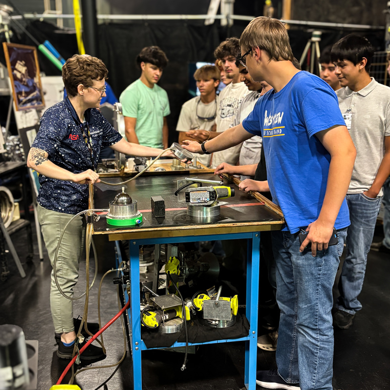 A NASA staff member demonstrates technical equipment for students as a Westview High School student interacts with the equipment during a hands-on learning session.