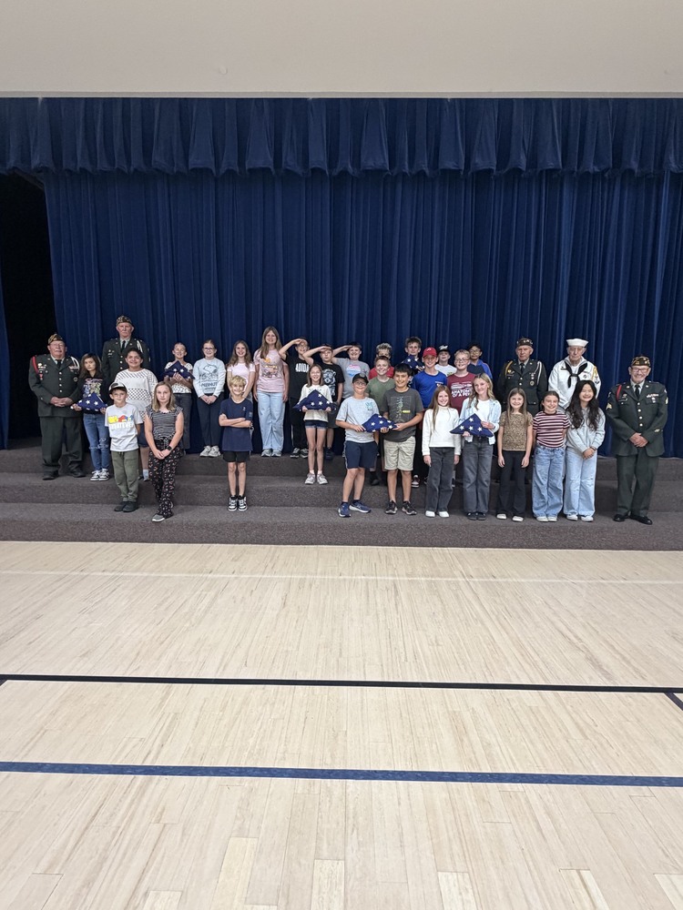 veterans standing with students who are saluting, smiling, and holding the flag