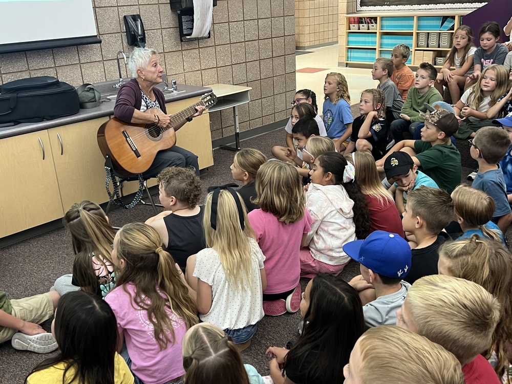 Picture of Kathy Vernieuw with her guitar singing with a group of second graders