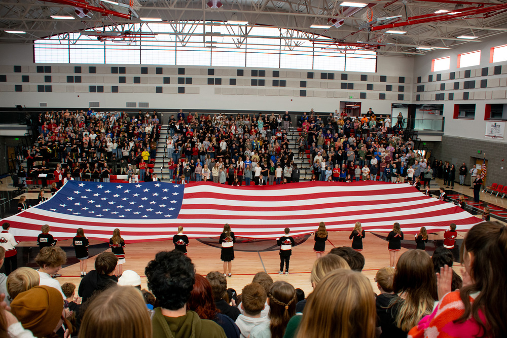 Photograph of Roy Jr presenting large AMerican flag at Veterans Day Assembly