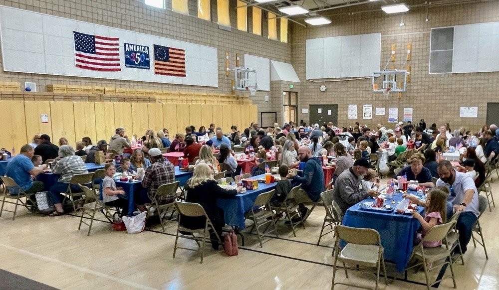 group of students and family members sitting at tables in the lunch room eating