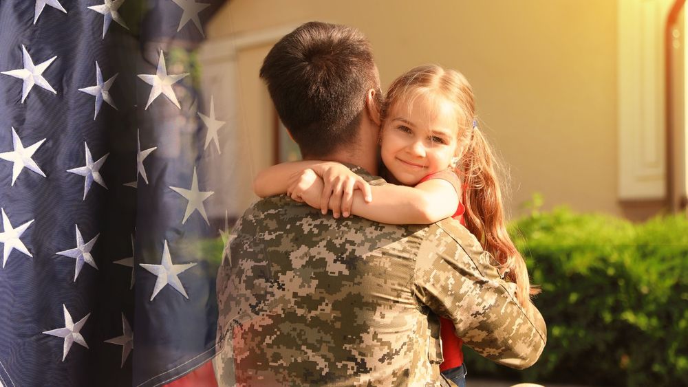 little girl hugging her dad who is in military uniform and an american flag