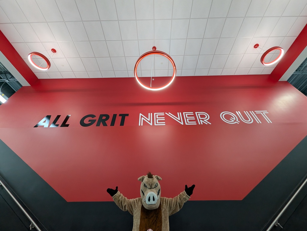Photo of our mascot, Raz with words on the wall saying "All Grit Never Quit"