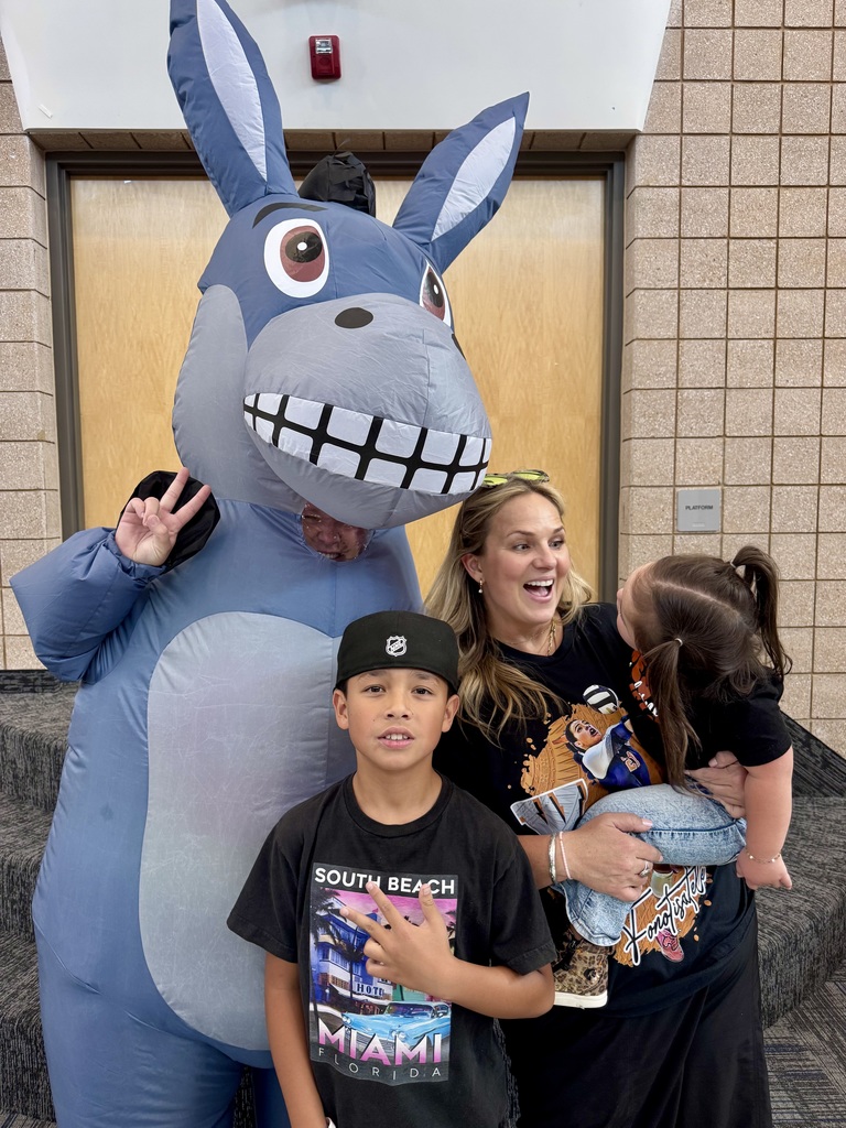 a family posing with Miss G wearing a donkey costume. the mom is laughing and the little girl in her arms is looking at the donkey, her son is smiling and doing a hand gesture