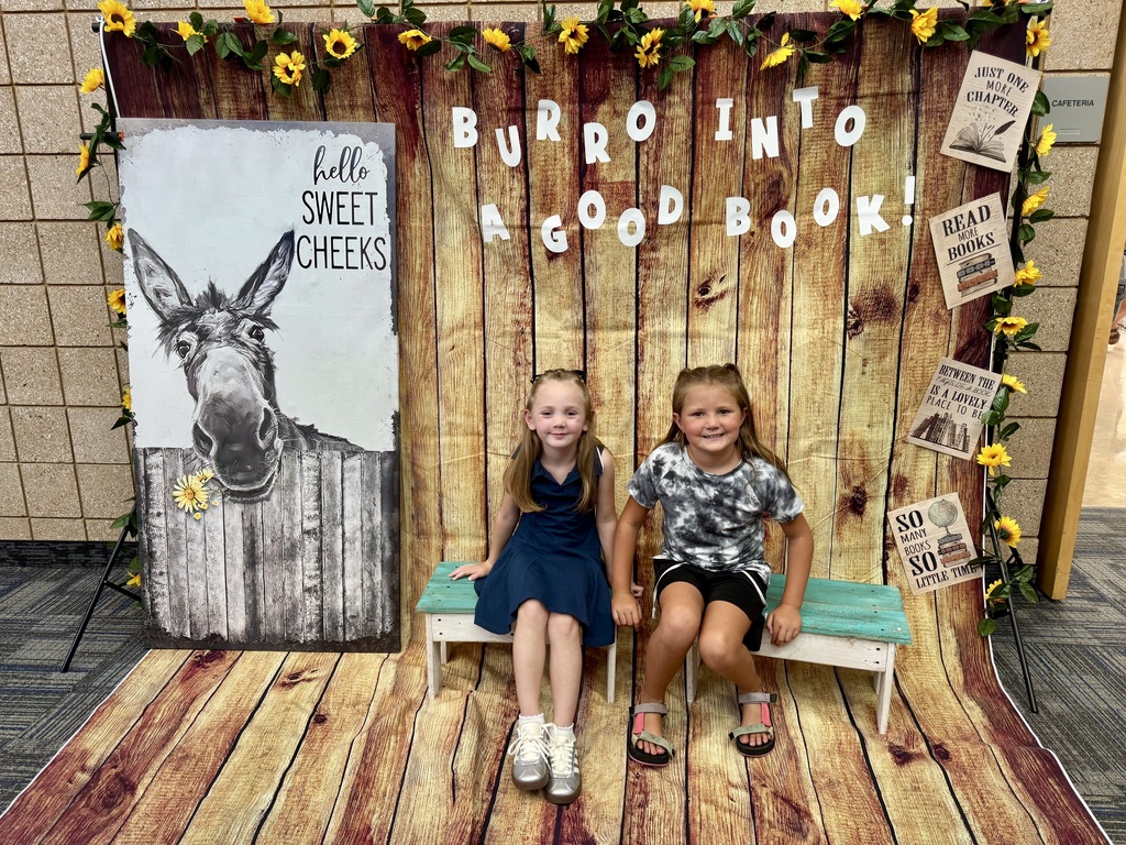 two students smiling next to a donkey sign that says hello sweet cheeks and lettering above their heads that reads burro into a good book.
